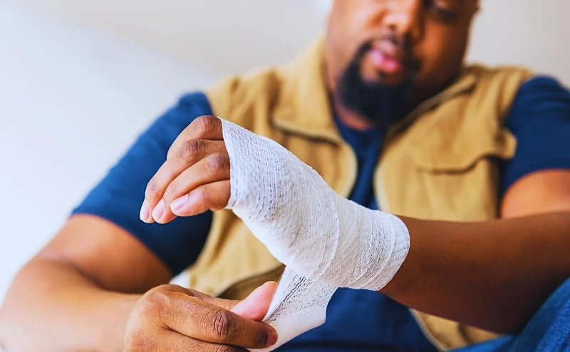 A man wrapping a white medical gauze bandage around his injured wrist. faking a work injury